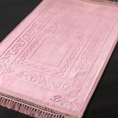 a close up of a pink towel on a black surface with an intricate design and fringe