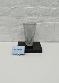 a clear glass sitting on top of a black stand next to a white brick wall