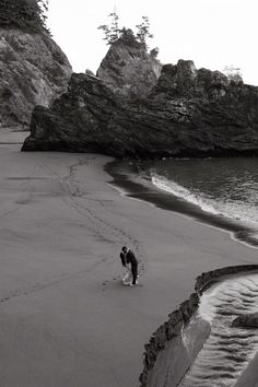 a person standing on top of a beach next to the ocean with rocks in the background