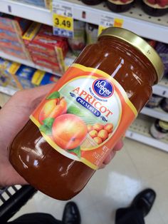 a hand holding a jar of peach jam in a grocery store's produce aisle