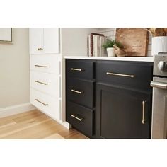 a kitchen with black and white cabinets, gold handles and brass pulls on the drawers