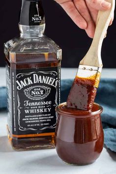 someone is holding a wooden spoon over a jar of jack daniels barbecue sauce with a bottle in the background