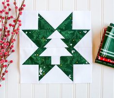 a green and white quilted christmas tree block next to some red berries on a table