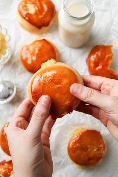 a person holding an orange doughnut in front of other pastries and condiments