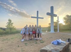 a group of young women standing in front of a large cross on top of a field