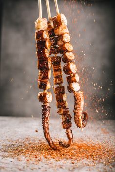 the skewers are being cooked on the grill with some spices flying around them