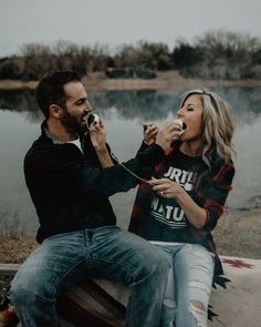 a man and woman sitting next to each other on a bench eating food by the water