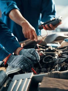 two people working on an engine in a car, one holding a remote control and the other pointing at it