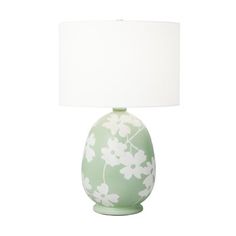 a green vase with white flowers on it and a white lamp next to it in front of a white background