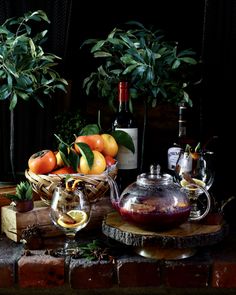 a table topped with oranges next to a glass vase filled with wine and fruit