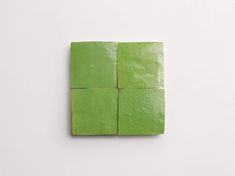 four square pieces of green paper sitting on top of a white surface with water droplets