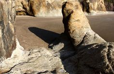 a large rock sitting on top of a beach next to a rocky cliff face covered in sand