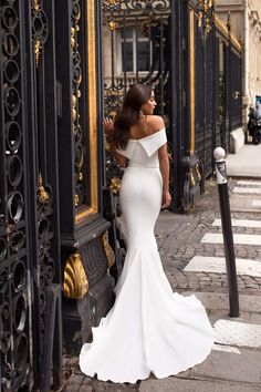 a woman in a white wedding dress leaning against a black iron fence with her back to the camera