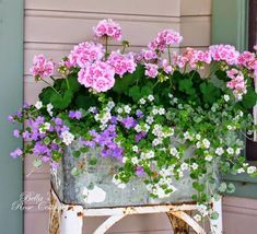 pink and white flowers in a metal planter on an old chair outside a house