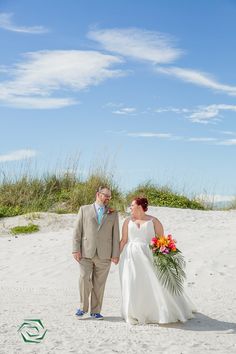 a bride and groom holding hands on the beach in front of some sand dunes with grass