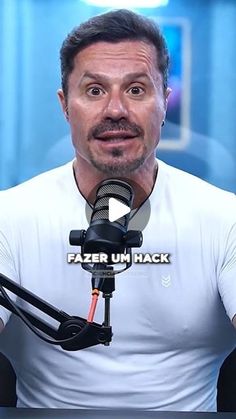 a man in white shirt sitting at a table next to a microphone with the words fazer um hack on it