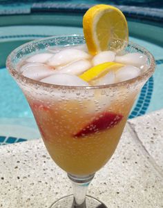 a drink with ice and lemon wedges sitting on a table next to a swimming pool