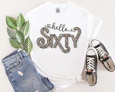 a white shirt with the words hello sixty on it next to two pairs of jeans