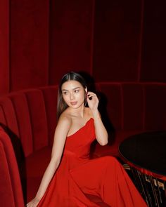 a woman in a red dress is sitting on a chair and talking on the phone