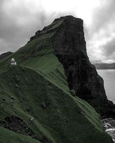 a small house on the side of a hill by the ocean under a cloudy sky