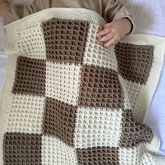 a baby laying on top of a bed covered in a crocheted checkered blanket