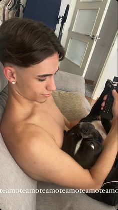 a shirtless man holding a black and white dog in his arms while sitting on a couch