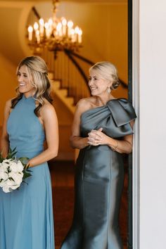 two women in blue dresses are smiling and looking at each other as they walk out the door