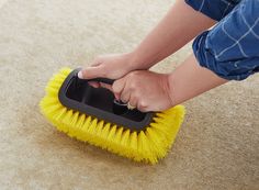 a person is cleaning the carpet with a yellow scrubbing brush on top of it