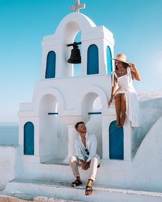 a man and woman sitting on the side of a white building with a bell tower