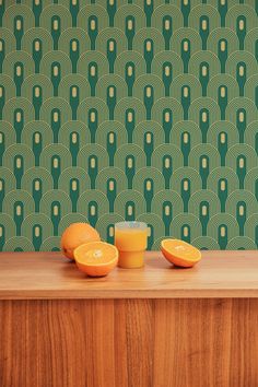 two oranges sitting on top of a wooden counter next to a green wallpaper