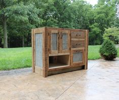 a wooden cabinet sitting on top of a cement floor next to a lush green field