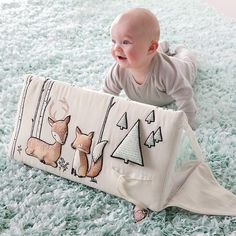 a baby laying on the floor next to a pillow that has deer and trees on it