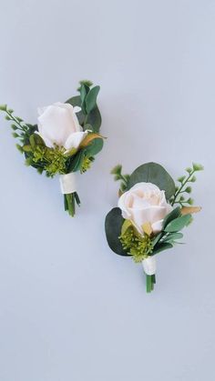 two white roses and greenery are placed on the side of each other, with green leaves