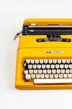 an old fashioned yellow typewriter sitting on top of a white table with words written below it