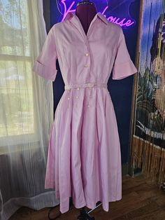 Smart pink Basila vintage dress with belt, likely from the 60's.  Belted with a 3-button closure.  Buttons galore on this posh dress; you will catch eyes for sure! Measurements taken while garment is laying flat: Sleeve (seam to end) - 11" Chest - 17" Waist - 14.5" Back of gown (nape to hem) - 43" Vintage sizes are different than modern sizing, so please review the measurements listed, double them, and measure your body to ensure a decent fit. Please note, items in my shop are vintage and pre-owned.  Some garments will have imperfections, and I do my best to note those in my listing and pictures.  If you have questions, please email me on the item and I will do my best to address them. Some items may be creased in shipping.  Please email me if you aren't sure how to address any wrinkles th Vintage Belted Dresses For Work, Pink Belted Midi Dress For Daywear, Pink Midi Dress With Button Closure For Daywear, Vintage Belted Workwear Dresses, 1950s Style Knee-length Dress With Button Closure, Vintage Midi-length Belted Dress, Vintage Pink Midi Dress With Short Sleeves, Vintage Midi Belted Dress, Pink Short Sleeve Vintage Midi Dress