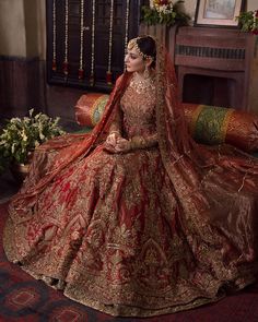 a woman sitting on top of a couch wearing a red and gold wedding dress with an elaborate