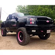 a black truck with pink rims parked in the dirt