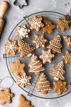 gingerbread cookies decorated with icing on a cooling rack next to cinnamon sticks and christmas decorations