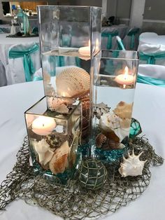 three glass vases with seashells and candles in them on a table at a wedding