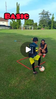 two young men are playing soccer in the grass with one man kneeling down to kick the ball