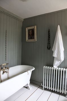 a white bath tub sitting next to a radiator and a painting on the wall