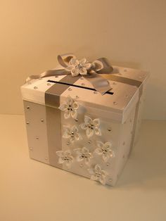 a white gift box with silver ribbon and flowers on the front, sitting on a table