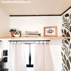 a shelf above a window in a room with white curtains and potted plants on it