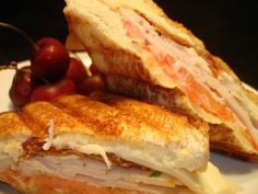 a sandwich cut in half sitting on top of a white plate next to grapes and cherries