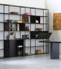 a black book shelf filled with books next to a desk and chair in front of a painting