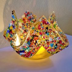 a yellow vase with many different colored glass beads on it's sides and a white wall in the background