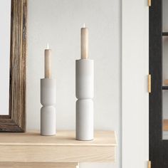 two white candles sitting on top of a wooden table next to a framed photo and mirror