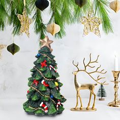 a small christmas tree next to a candle holder and other ornaments on a table with a white background