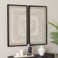 two white vases sitting on top of a black table next to a wall mounted art piece