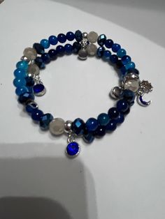 Introducing our stunning Blue Agate Memory Wire Bracelet with Sun, Moon, and Star Charm! This unique bracelet features beautiful blue agate beads that are known for their calming and balancing energies. The addition of the sun, moon, and star charms adds a touch of celestial beauty to this piece. Perfect for those who love the mystical and magical, this bracelet is the perfect accessory to add a pop of color and whimsy to any outfit. Handcrafted with care and attention to detail, this bracelet is a true statement piece that is sure to turn heads. Add a touch of celestial magic to your jewelry collection with this enchanting bracelet! Blue Moonstone Beaded Bracelets With Gemstone Beads, Handmade Blue Moonstone Beaded Bracelets, Blue Moonstone Beaded Bracelets Gift, Handmade Blue Moonstone Bracelets, Gift Blue Moonstone Beaded Bracelets, Blue Round Spiritual Charm Bracelet, Handmade Blue Round Crystal Bracelet, Blue Beaded Agate Bracelets, Blue Spiritual Bangle Stretch Bracelet